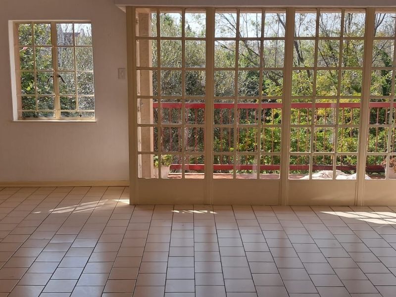 An empty living room featuring tiled flooring and large grid-pattern glass doors that open onto a balcony with garden views.