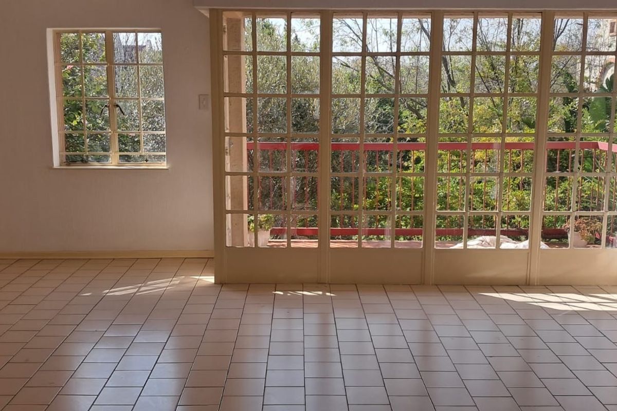 An empty living room featuring tiled flooring and large grid-pattern glass doors that open onto a balcony with garden views.