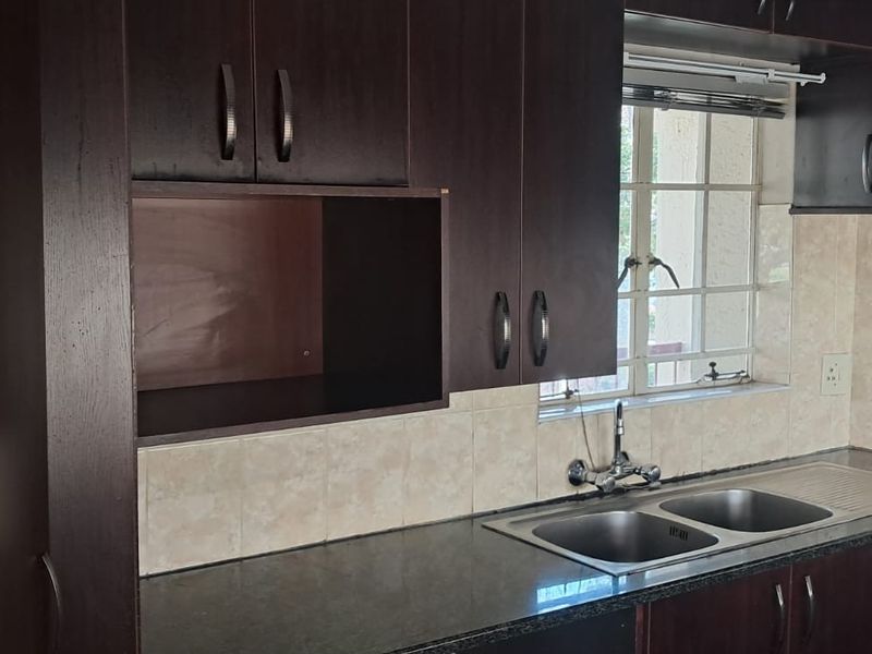 A functional kitchen featuring dark wood cabinetry, laminate countertops, a double stainless steel sink, and a tiled backsplash.
