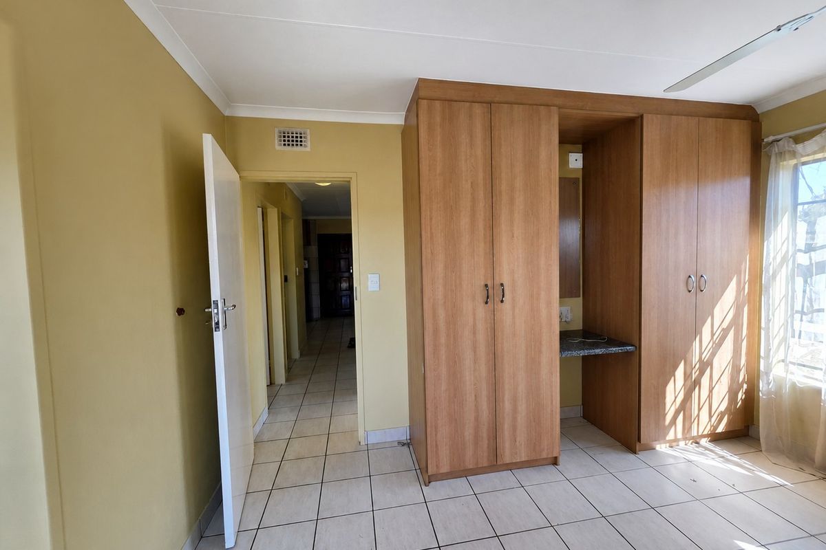 A spacious bedroom featuring neutral walls, tiled flooring, and extensive built-in wooden cupboards with an integrated vanity area.