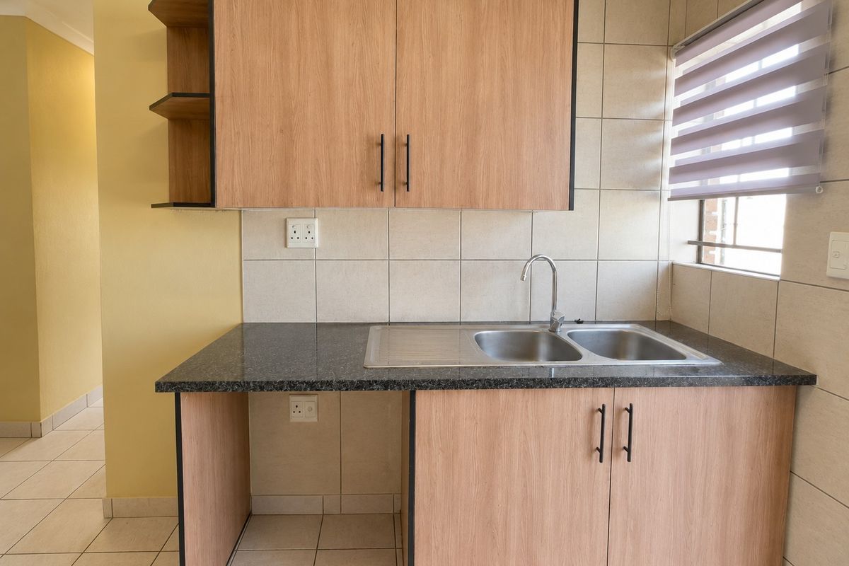 A clean and functional kitchen area featuring light wood-look cabinetry, granite countertops, a double stainless steel sink, and neutral tiled finishes.