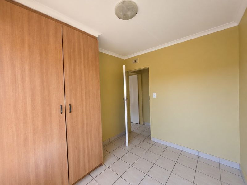 A clean, empty bedroom featuring neutral tiled flooring, built-in wooden wardrobes, and yellow-toned walls, offering a blank canvas for personalization.