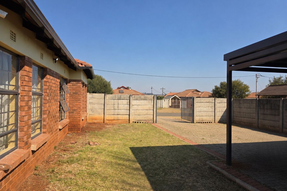 Rear exterior view featuring a face brick house, paved driveway, carport, and enclosed yard with precast concrete boundary walls.