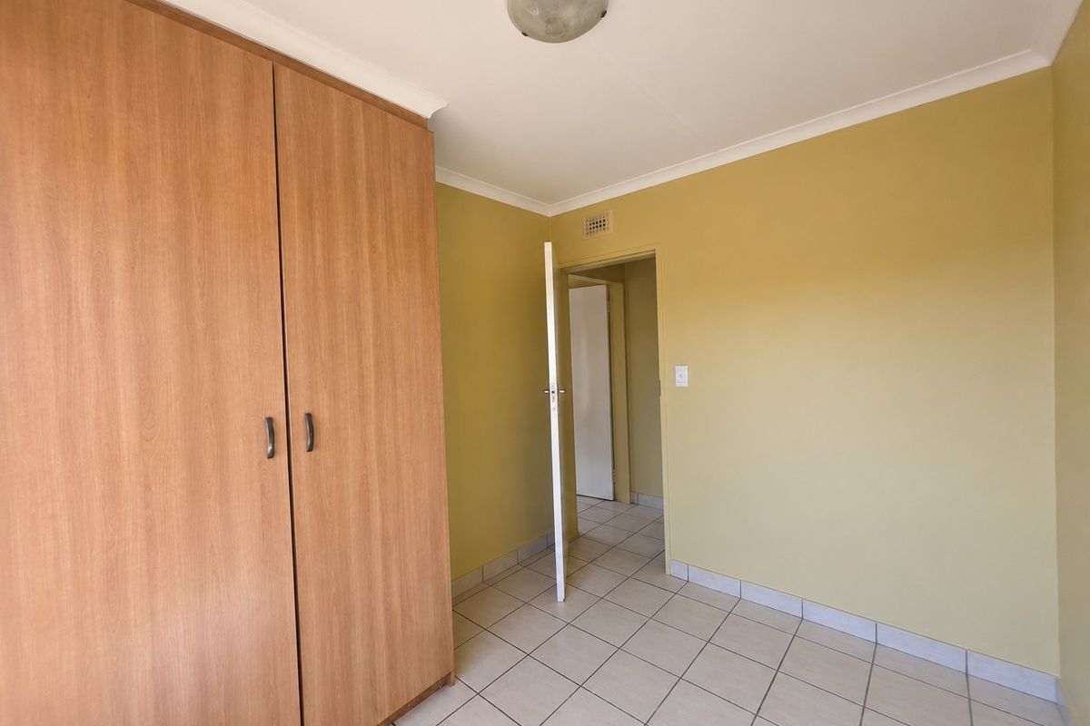 A clean, empty bedroom featuring neutral tiled flooring, built-in wooden wardrobes, and yellow-toned walls, offering a blank canvas for personalization.