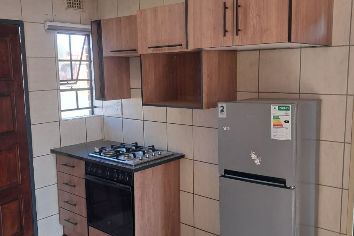 Compact kitchen featuring wood-look cabinetry, a built-in gas hob and oven, and full-height wall tiling.