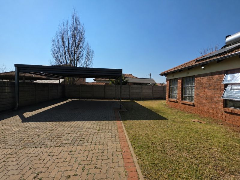 Rear exterior view featuring a paved driveway with a covered carport, brick wall construction, and a well-maintained lawn area.