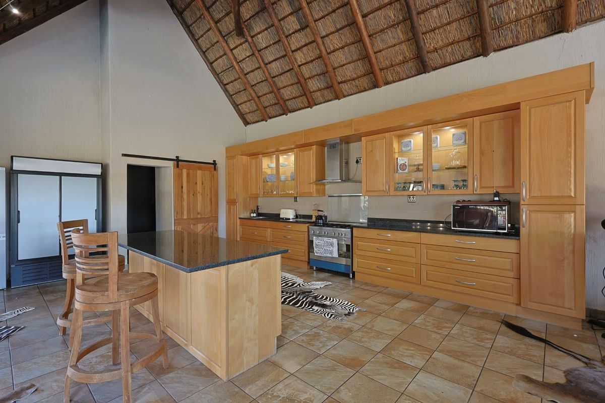 Spacious kitchen featuring high exposed thatch ceilings, wooden cabinetry, granite countertops, a central island, and a gas stove in a rustic farm setting.