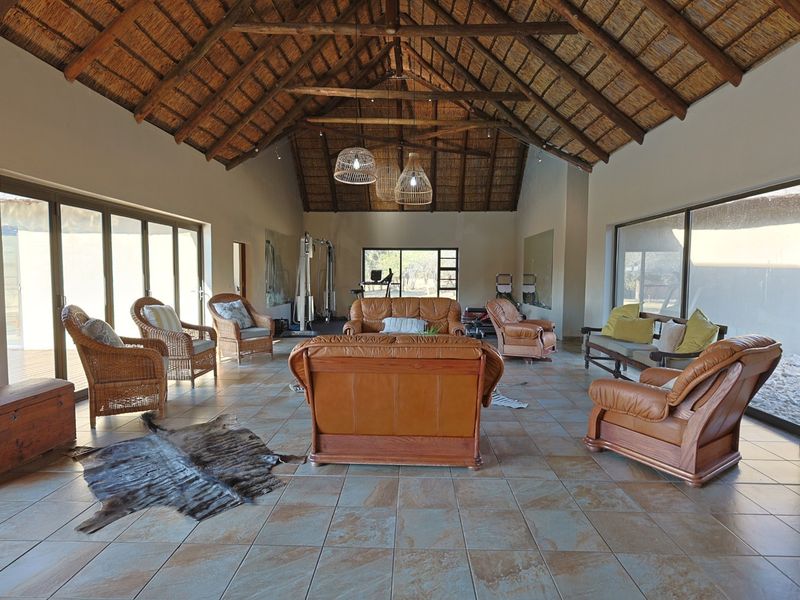 Spacious living area featuring a high vaulted thatched roof with exposed timber trusses, tiled flooring, and large sliding glass doors providing ample natural light.