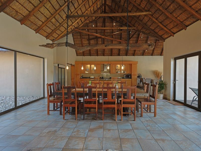 Spacious open-plan living and dining area featuring a high vaulted thatched ceiling with exposed timber trusses, ceramic tiled flooring, and integrated kitchen cabinetry.