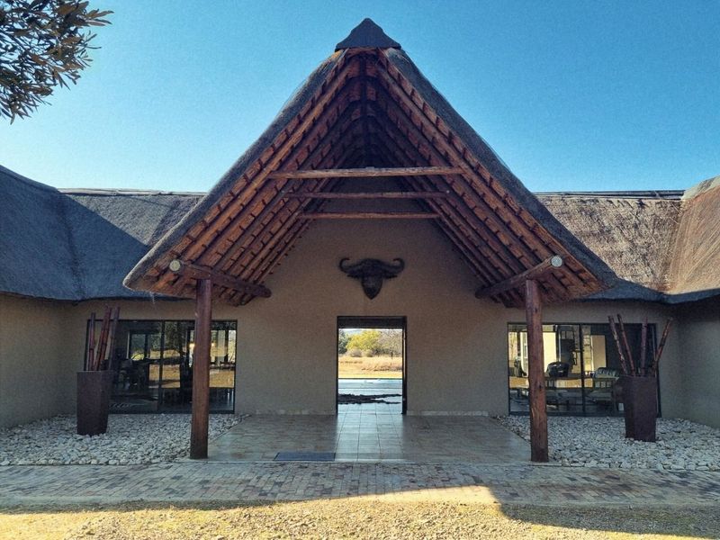 A striking farm-style entrance featuring a prominent thatched roof, timber support columns, and a tiled porch leading into the main living area.