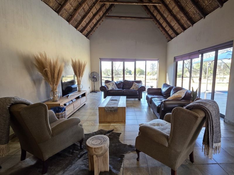 Spacious living room featuring a high vaulted thatched ceiling with exposed timber rafters, tiled flooring, and large sliding glass doors providing natural light.