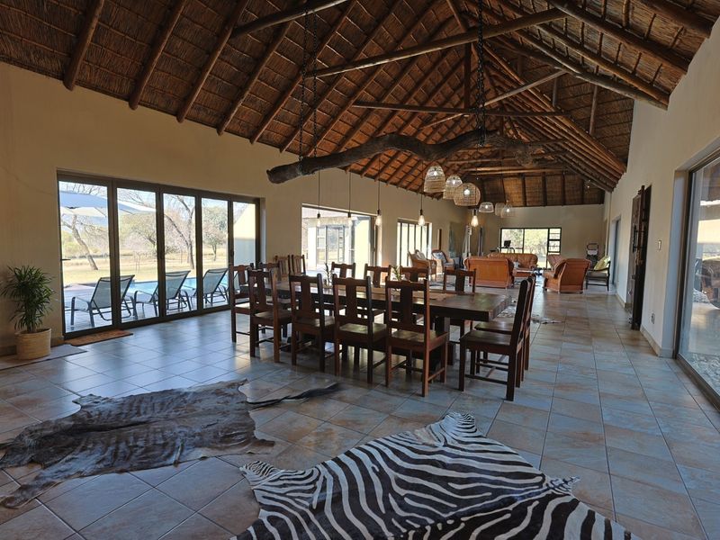Spacious open-plan living and dining area featuring a high vaulted thatched ceiling with exposed timber trusses and large sliding doors opening to the pool.