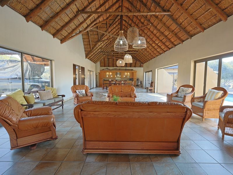 Spacious open-plan living area featuring a high vaulted thatched ceiling with exposed timber trusses, tiled floors, and large sliding doors opening to the exterior.