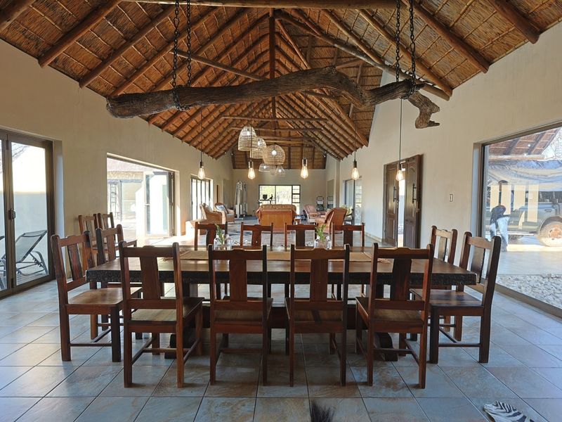 Spacious dining area featuring a high vaulted thatched ceiling with exposed timber trusses, tiled floors, and large sliding glass doors providing natural light.