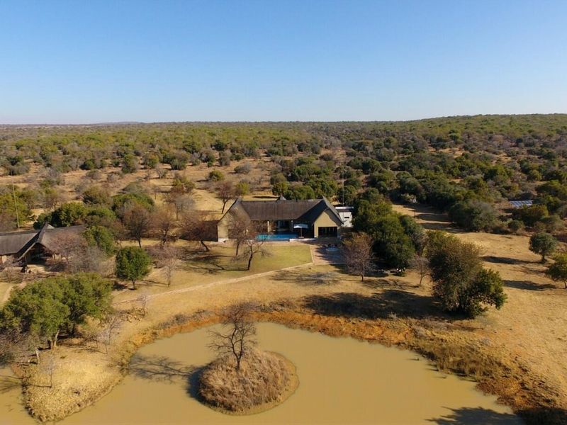Aerial view of a farm property featuring a main residence with a thatched roof, swimming pool, and a private dam set in expansive bushveld.