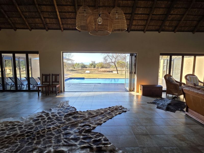 Spacious living area featuring a high thatched ceiling with exposed rafters, tiled floors, and large bi-fold doors opening onto a pool deck.
