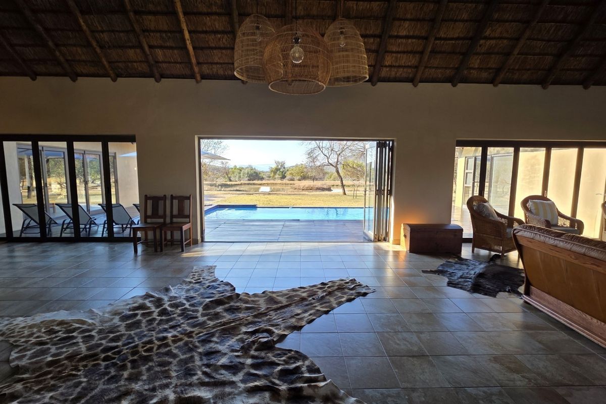 Spacious living area featuring a high thatched ceiling with exposed rafters, tiled floors, and large bi-fold doors opening onto a pool deck.