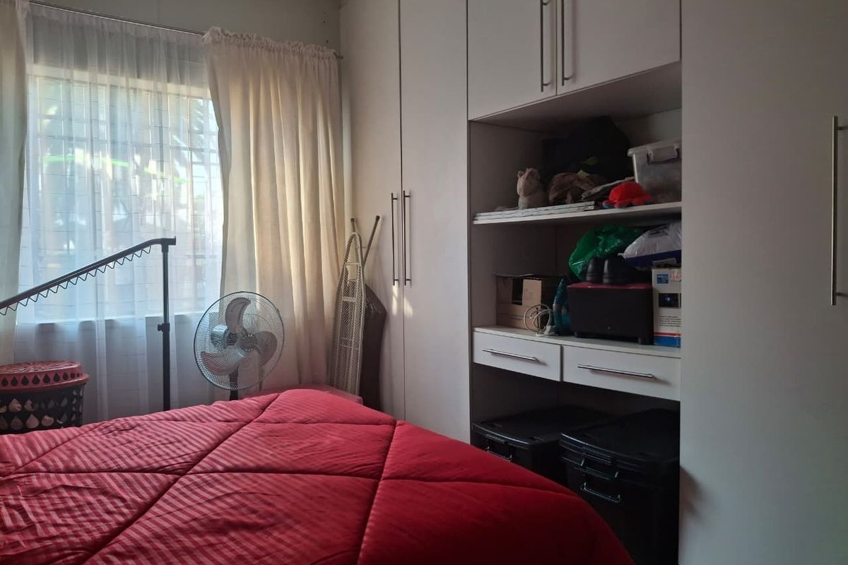 A bedroom featuring white built-in cupboards with integrated shelving and security bars on the window.