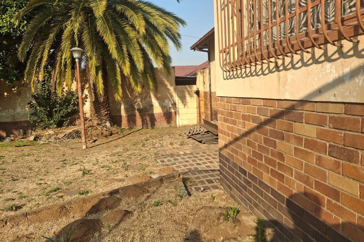 A rear exterior view of the property featuring a brick facade, security bars on windows, and a garden area with a paved walkway.