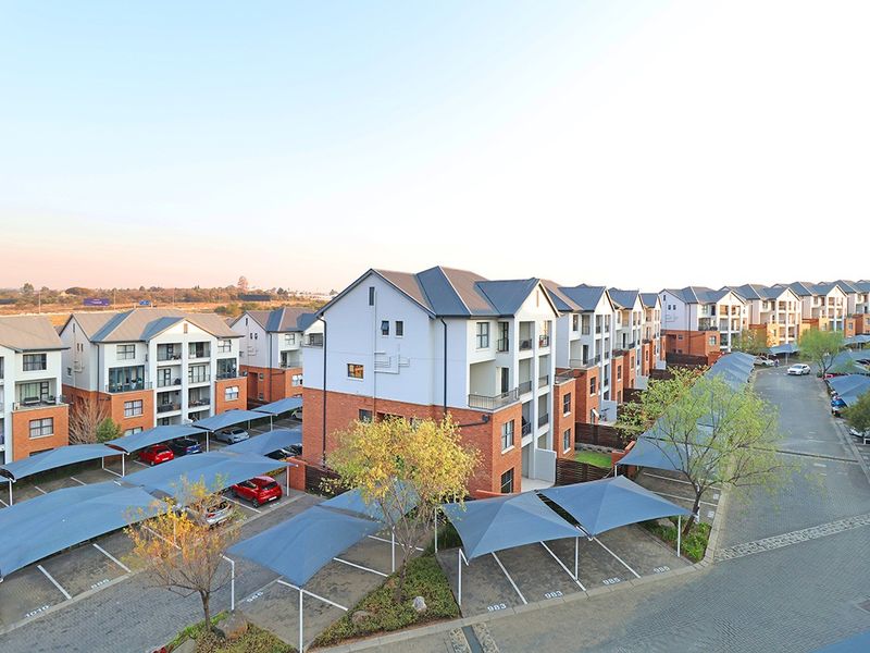 Aerial view of a modern apartment complex featuring multi-story residential buildings, paved driveways, and designated covered parking bays.