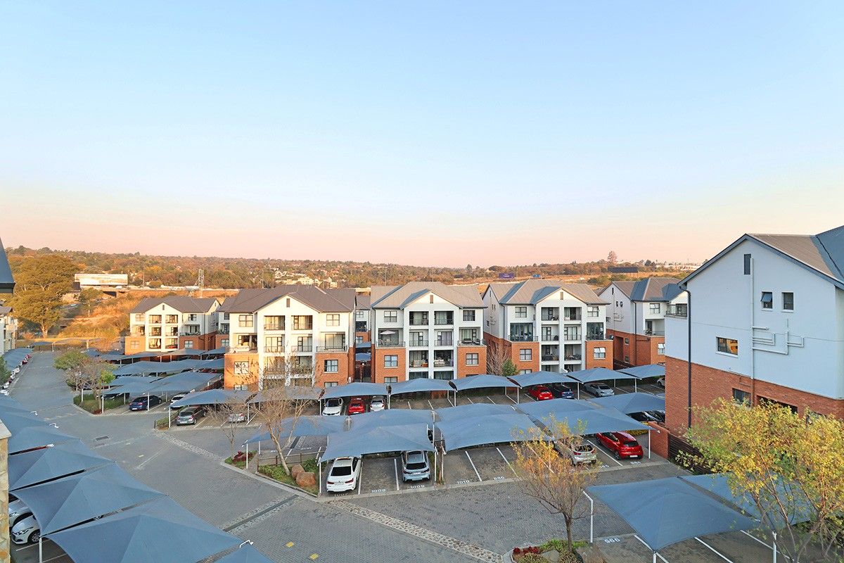 Aerial view of a residential apartment complex featuring multi-story buildings and extensive paved parking areas with shade cloth carports.