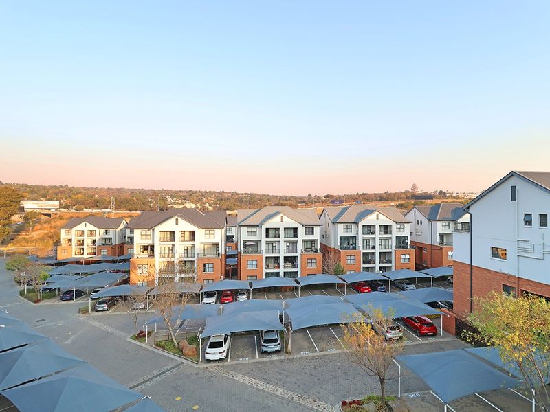 Aerial view of a residential apartment complex featuring multi-story buildings and extensive paved parking areas with shade cloth carports.