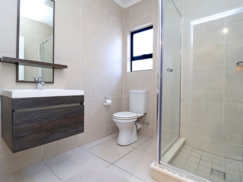 Modern bathroom featuring a wall-mounted vanity, glass shower enclosure, and neutral floor-to-ceiling tiling.