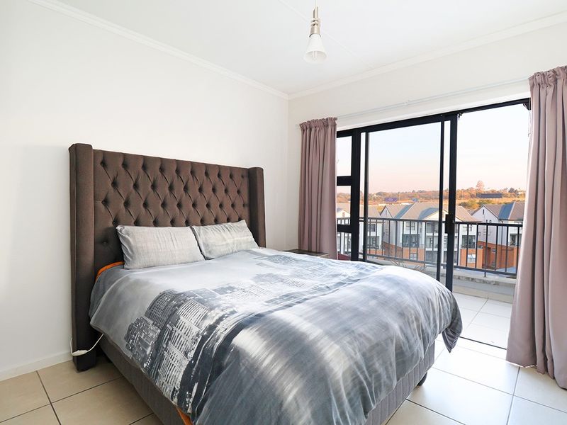 A bright bedroom featuring tiled flooring and a large sliding glass door that opens onto a private balcony with neighborhood views.