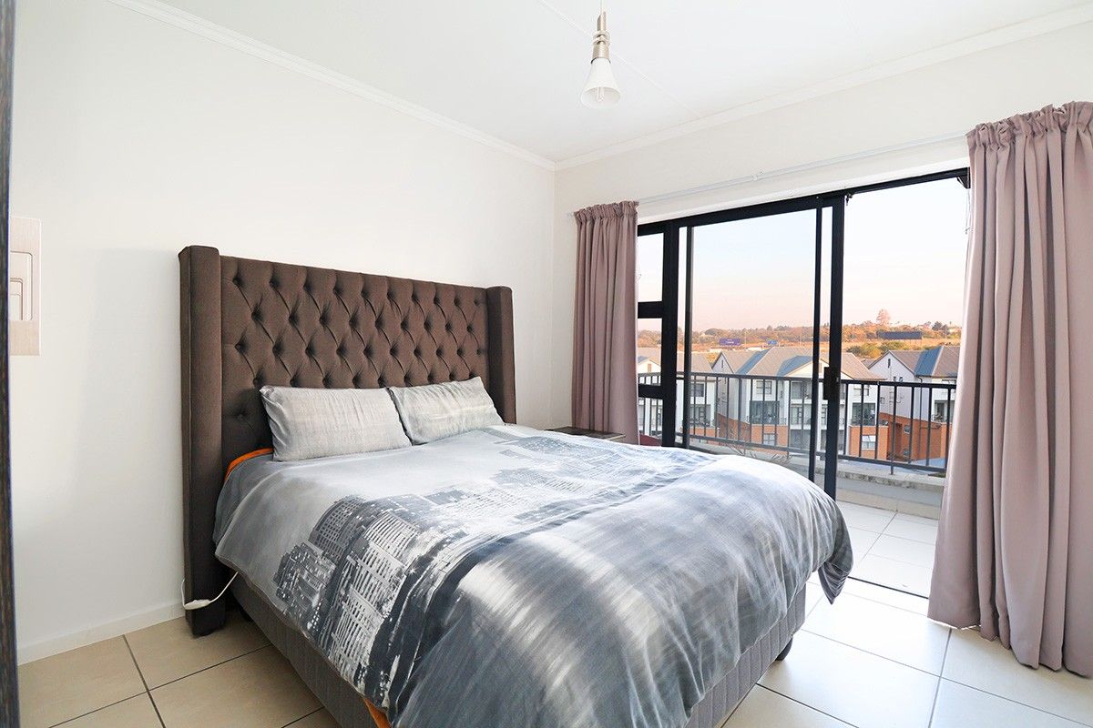 A bright bedroom featuring tiled flooring and a large sliding glass door that opens onto a private balcony with neighborhood views.