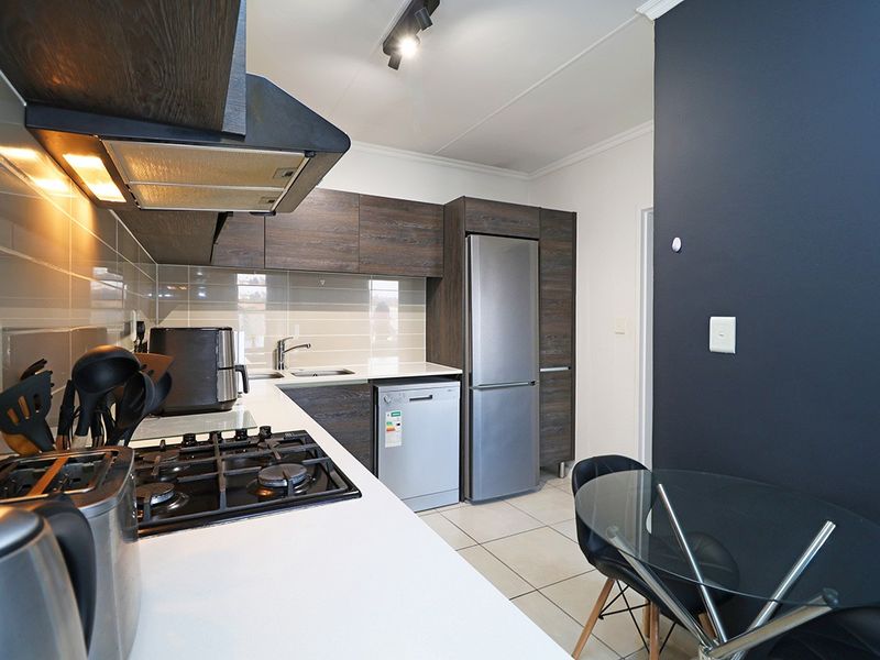 Modern kitchen featuring dark wood cabinetry, gas hob, extractor fan, tiled backsplash, and neutral floor tiles, offering a functional and contemporary cooking space.
