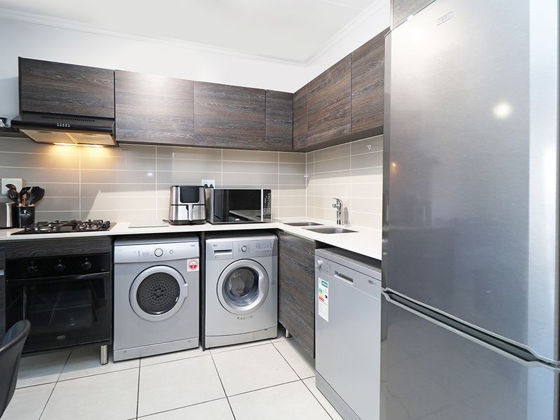 Modern kitchen featuring dark wood-grain cabinetry, stone-look countertops, tiled backsplash, gas hob, extractor fan, and integrated space for multiple appliances.