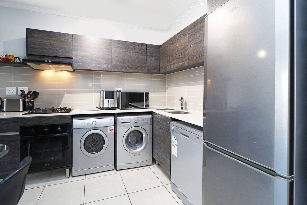Modern kitchen featuring dark wood-grain cabinetry, stone-look countertops, tiled backsplash, gas hob, extractor fan, and integrated space for multiple appliances.