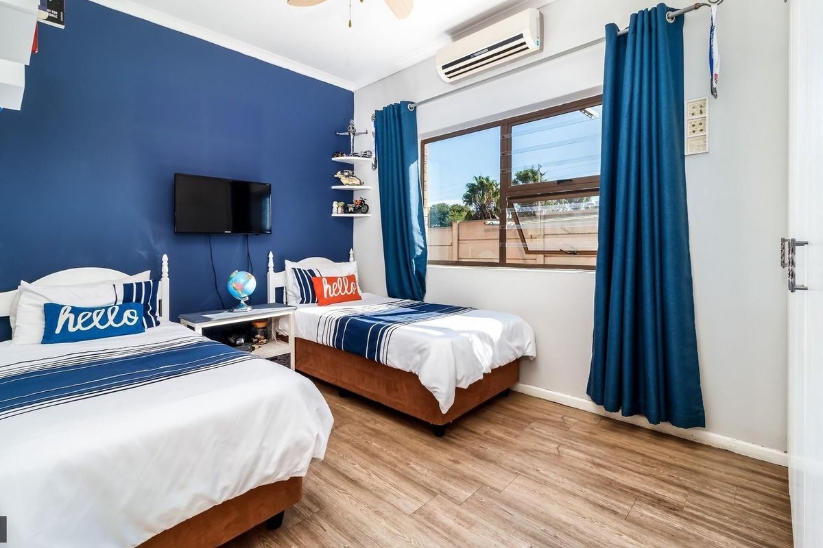 A well-maintained bedroom featuring laminate flooring, a split-system air conditioner, and a ceiling fan, with a large window providing natural light.