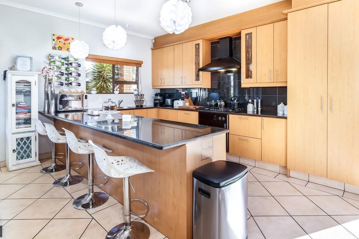A functional kitchen featuring light wood cabinetry, dark granite countertops, a gas hob with extractor fan, and tiled flooring with a breakfast bar island.
