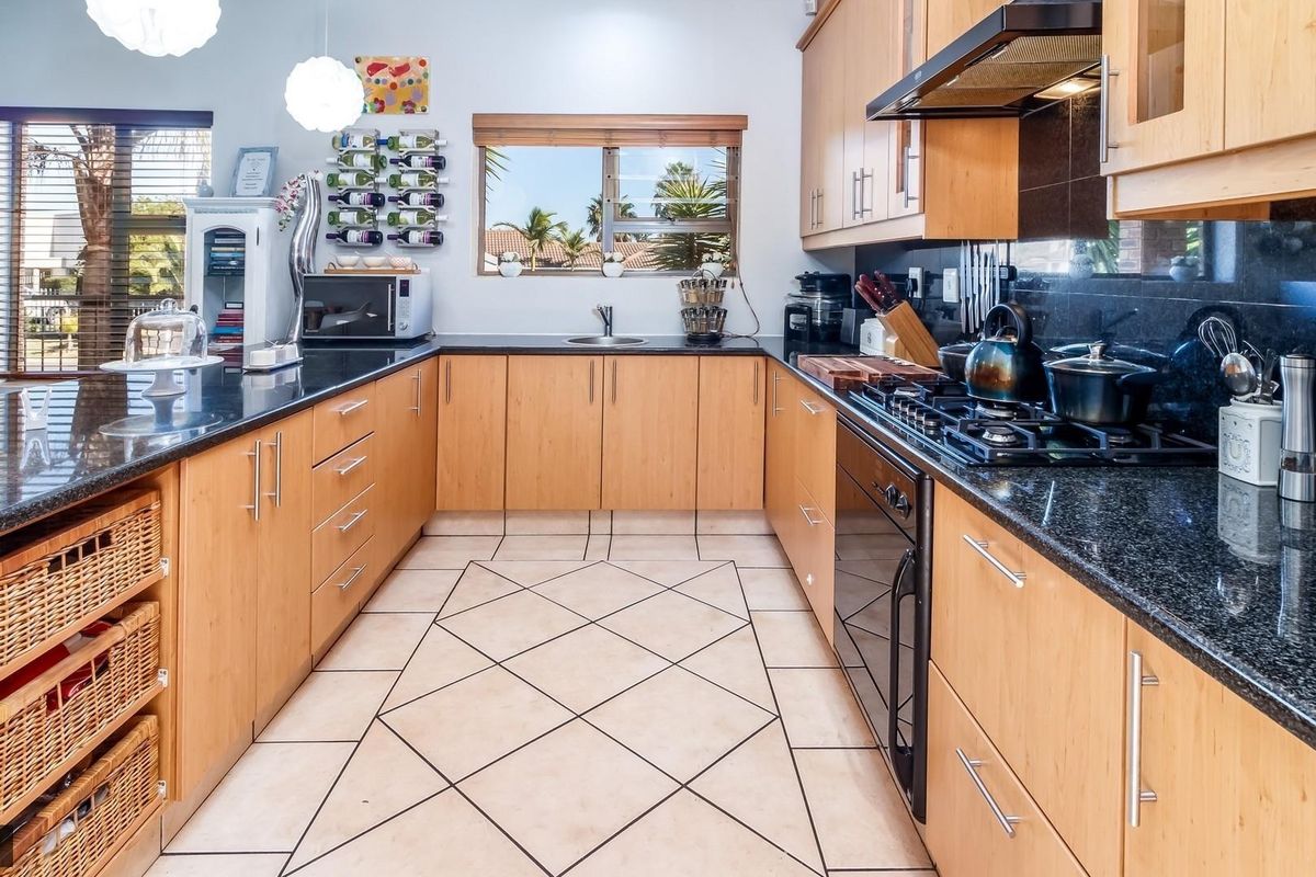 A functional kitchen featuring light wood cabinetry, dark granite countertops, a gas hob, and tiled flooring with a neutral layout.