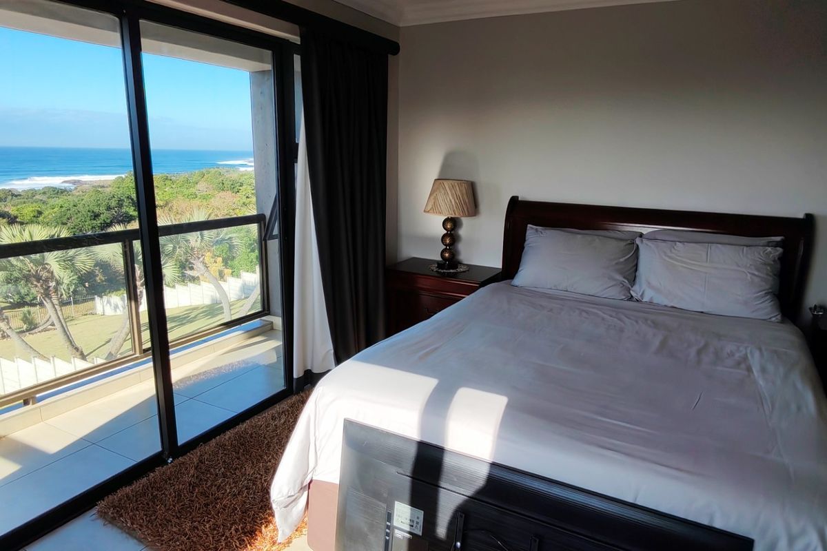 A well-maintained bedroom featuring a sliding glass door that opens onto a balcony with scenic ocean and coastal views.