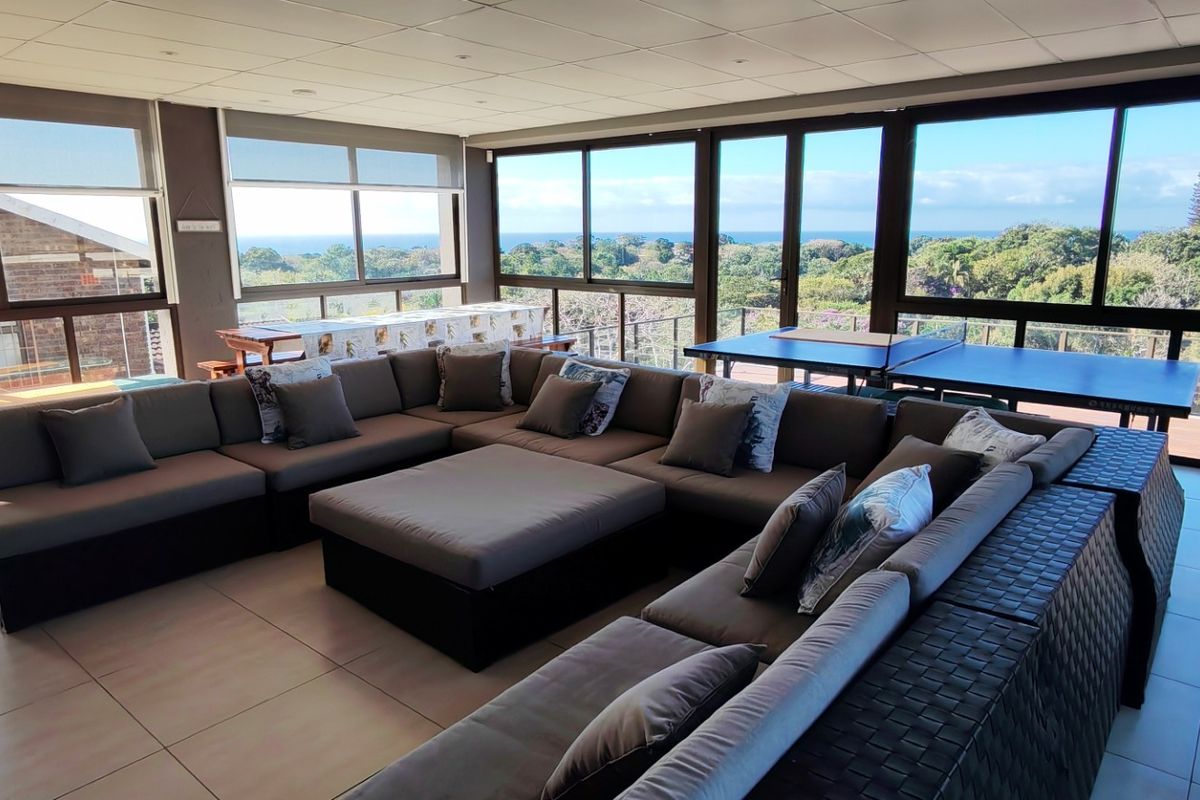 Spacious living area featuring extensive aluminium sliding windows with panoramic coastal and garden views, tiled flooring, and recessed ceiling lighting.