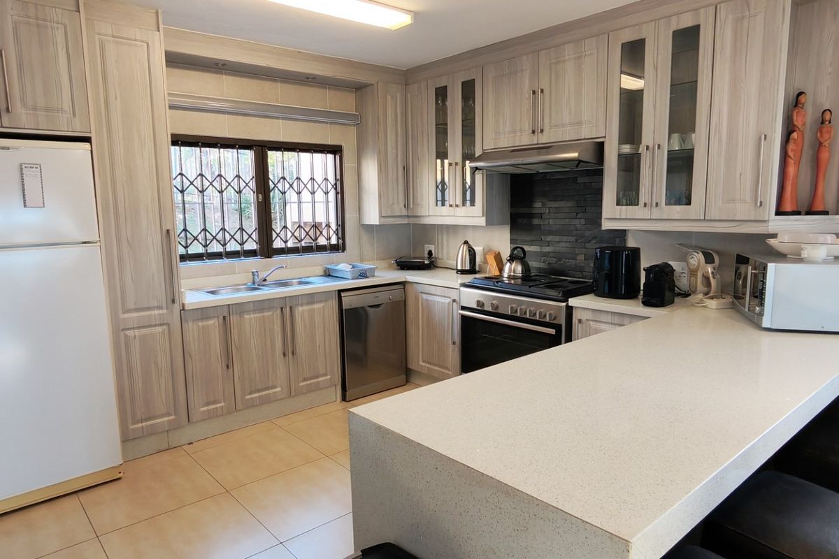 A well-maintained kitchen featuring light wood-grain cabinetry, stone countertops, a breakfast bar, and a gas stove with an integrated extractor fan.
