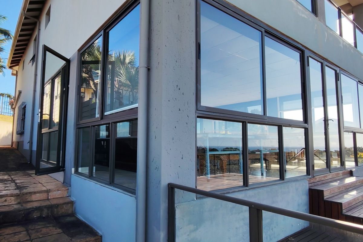 Rear exterior view of the property featuring extensive glass sliding doors, timber decking, and concrete stairs leading to the garden area.