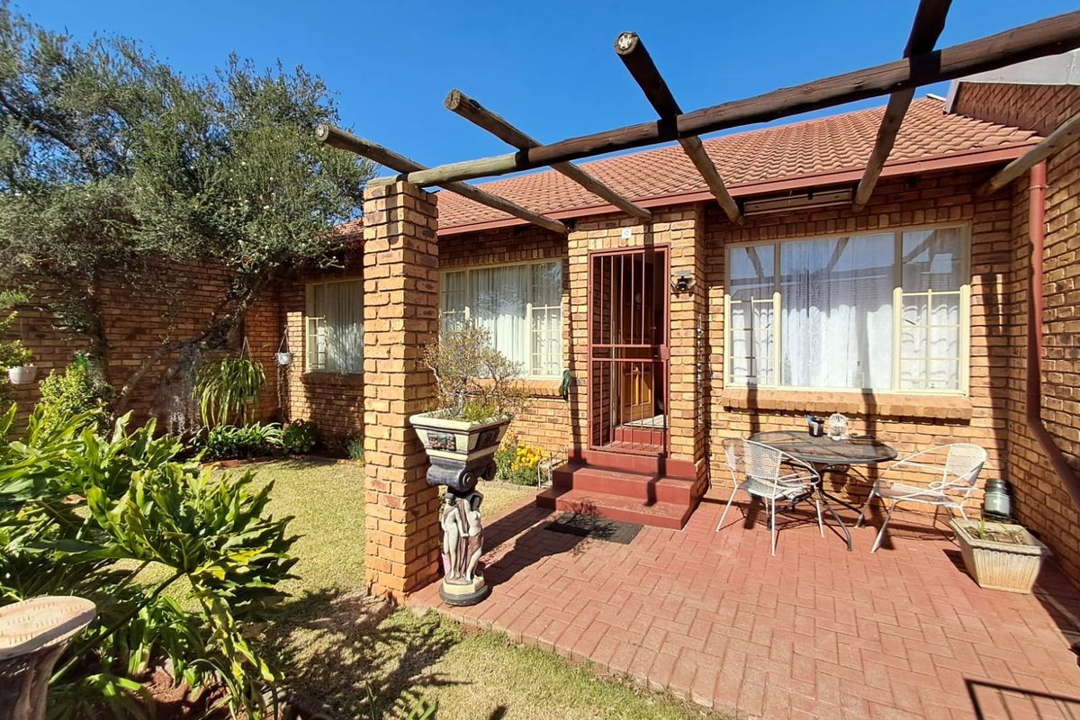 A rear exterior view of the townhouse featuring a brick facade, a paved patio area, and a timber pergola structure overlooking a private garden.