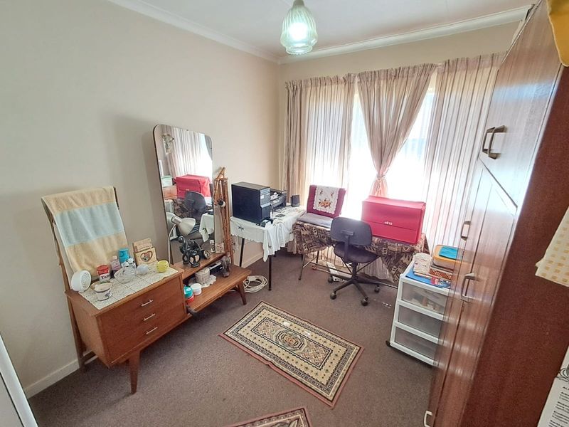 A functional bedroom featuring carpeted flooring, neutral wall finishes, and large windows with curtain rails, offering a versatile space for rest or home office use.