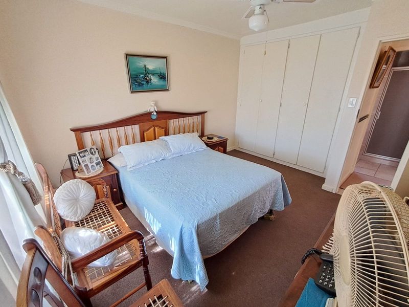 A carpeted bedroom featuring built-in cupboards and a ceiling fan, offering a functional and well-maintained living space.