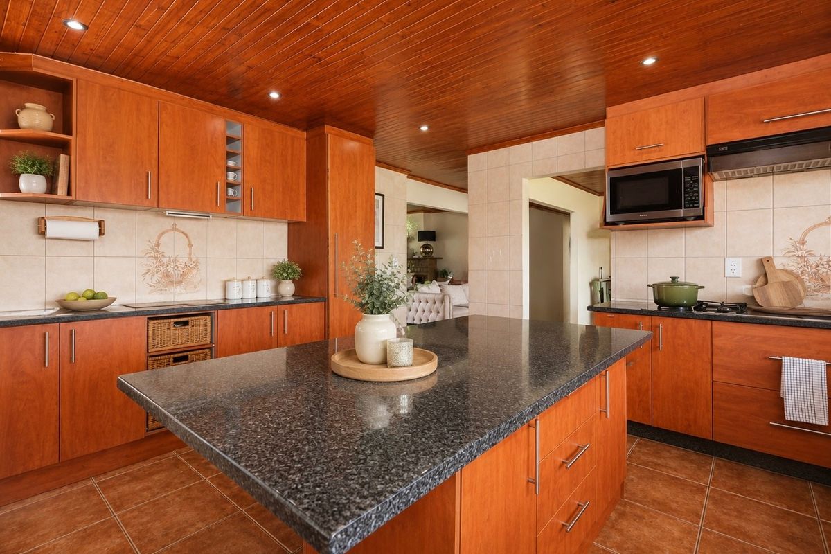A well-maintained kitchen featuring warm timber cabinetry, a central granite-topped island, tiled flooring, and a distinctive timber-paneled ceiling with recessed lighting.