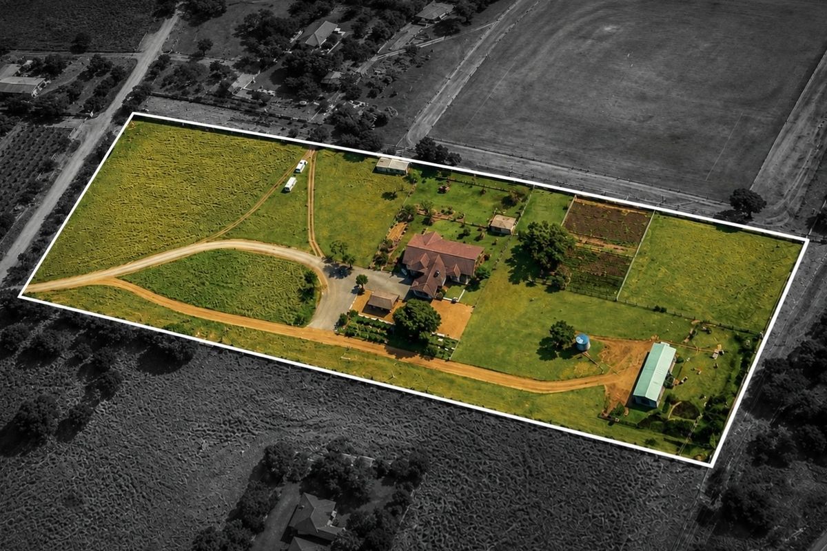 Aerial view of a large farm property featuring a main residence, multiple outbuildings, expansive grounds, and a gravel driveway network.