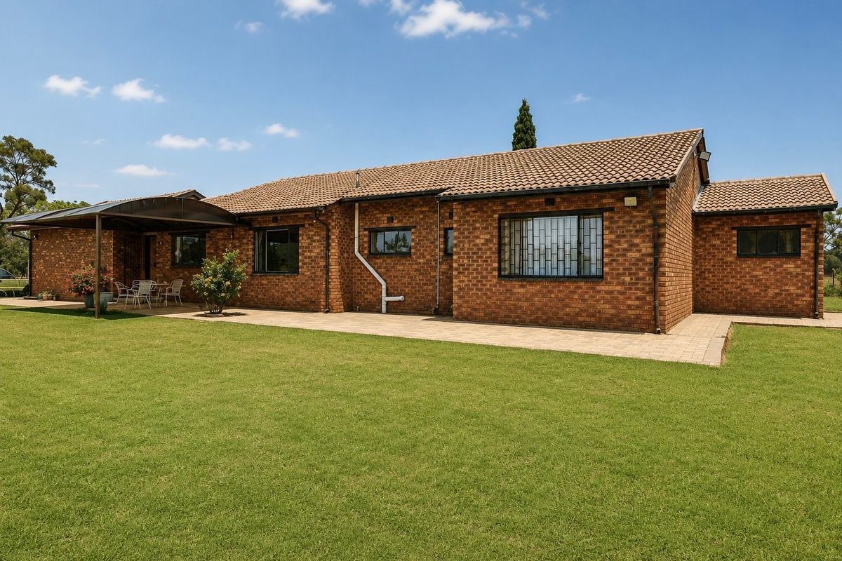 Rear view of a well-maintained brick farmhouse featuring a covered patio, paved outdoor area, and expansive lawn.
