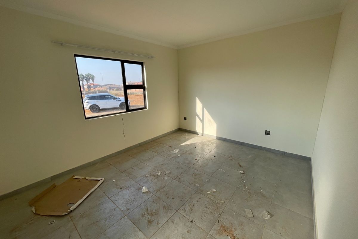 An empty bedroom featuring tiled flooring and an aluminium window frame, requiring minor repairs to the wall plaster and a thorough cleaning.