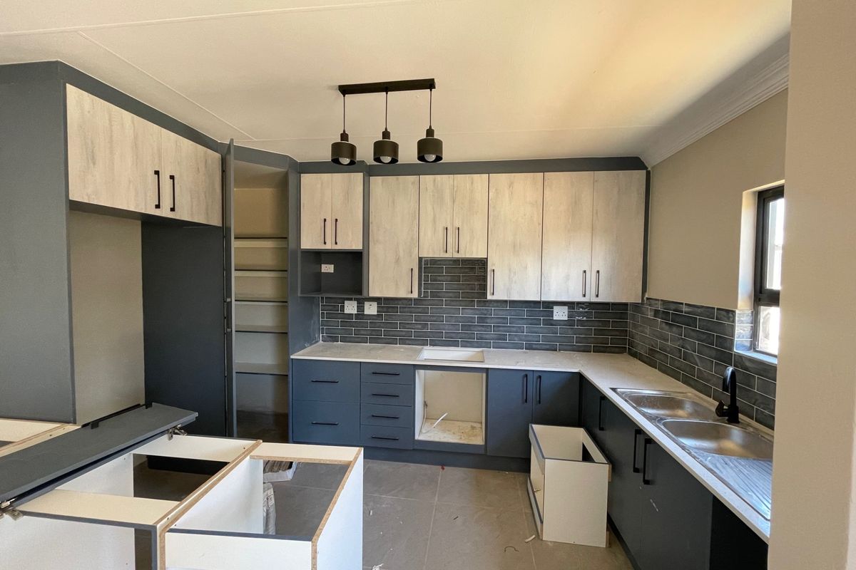 A modern kitchen featuring two-tone cabinetry, subway tile backsplash, and stone countertops, currently undergoing final installation and awaiting appliances.