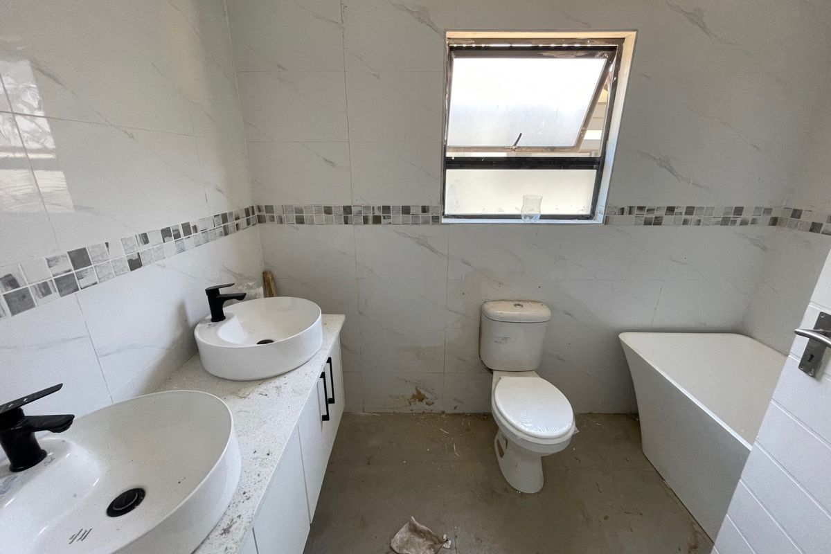 A bathroom featuring a double vanity with vessel sinks, a toilet, and a freestanding bathtub, currently requiring floor finishing and minor wall repairs.
