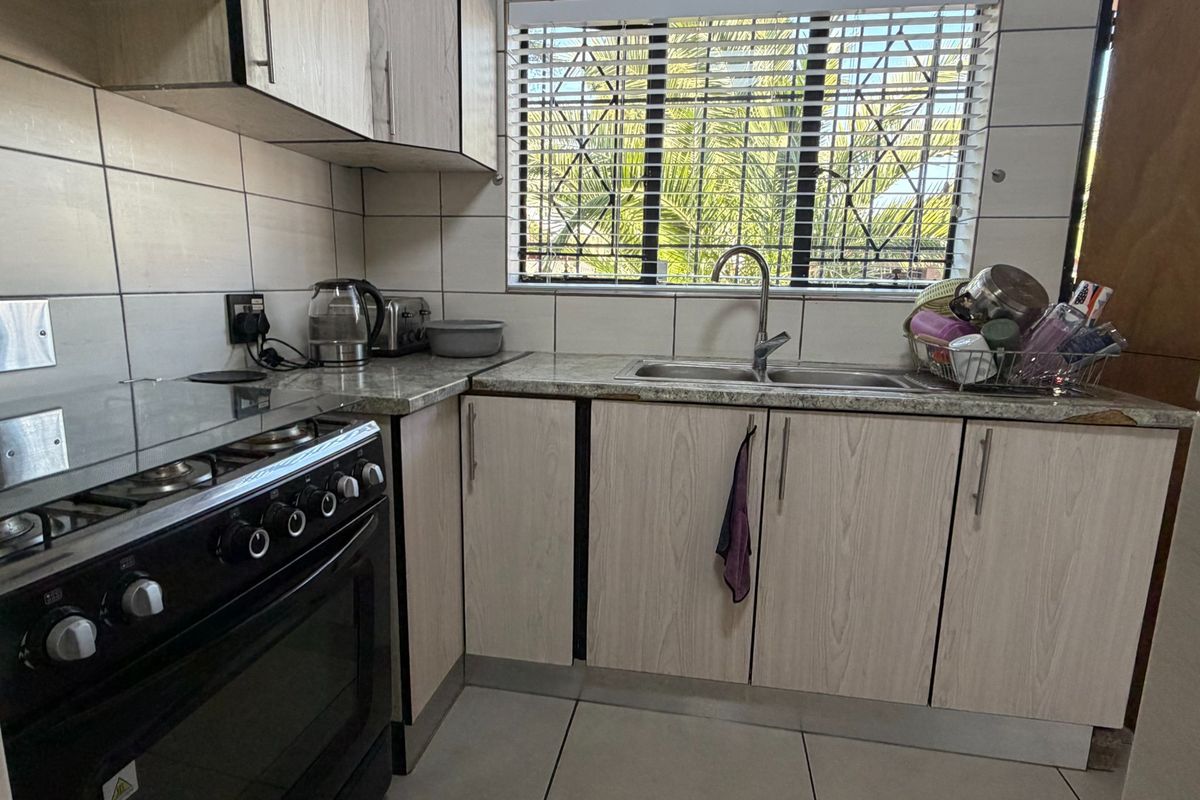 A functional kitchen featuring light wood-grain cabinetry, laminate countertops, a stainless steel double sink, and tiled finishes throughout.
