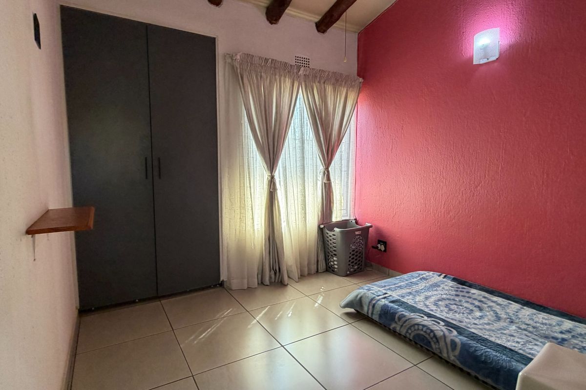 A bedroom featuring tiled flooring, exposed timber ceiling beams, and a built-in wardrobe, with a distinctive pink accent wall.
